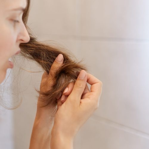 Closeup profile portrait of upset astonished woman looking at her dry hair, having problems, needs to change shampoo or special treatment at trichological clinic.